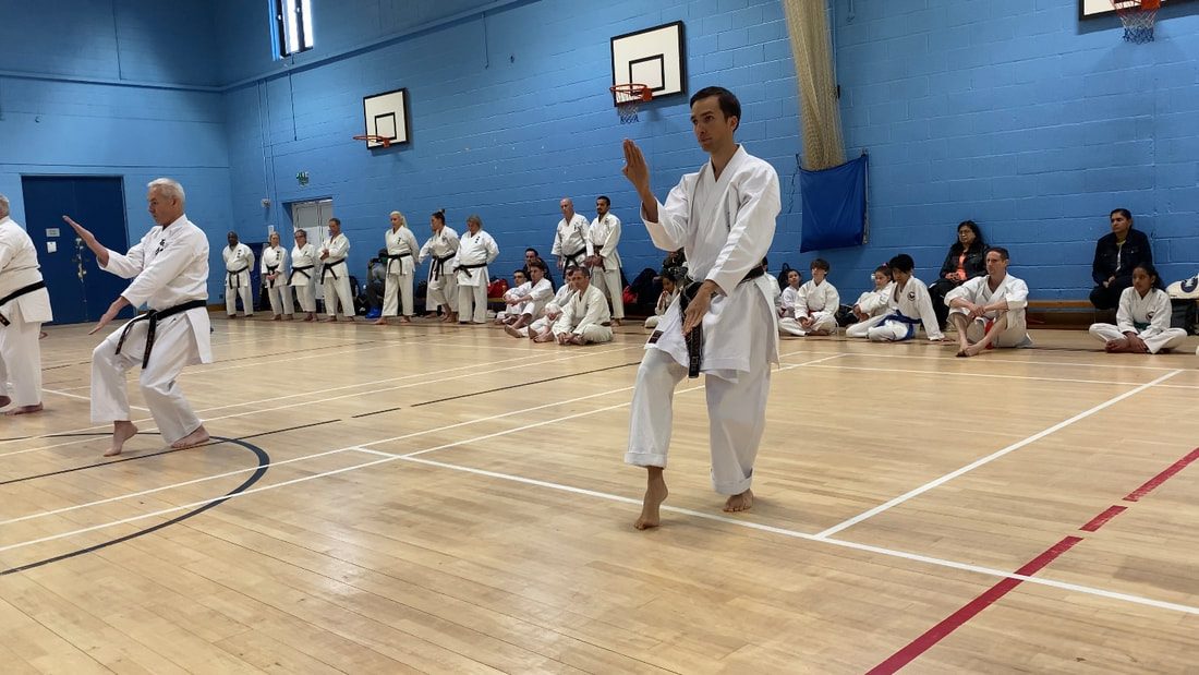 An instructor demonstrates a technique while the class watches from the side of the hall