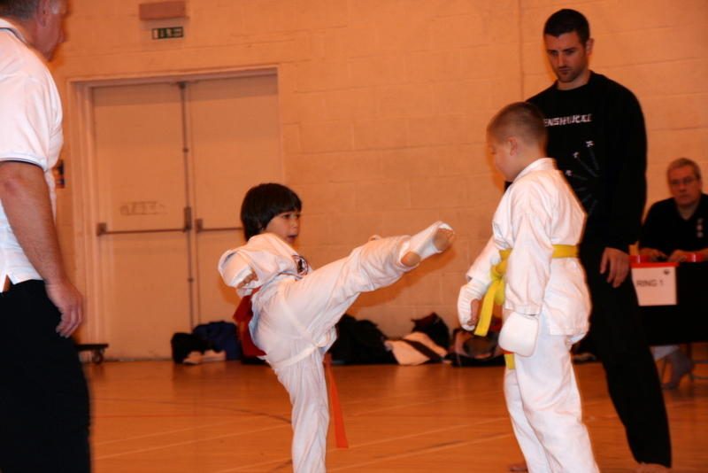 A young student kicks a pad held by an instructor while a classmate watches