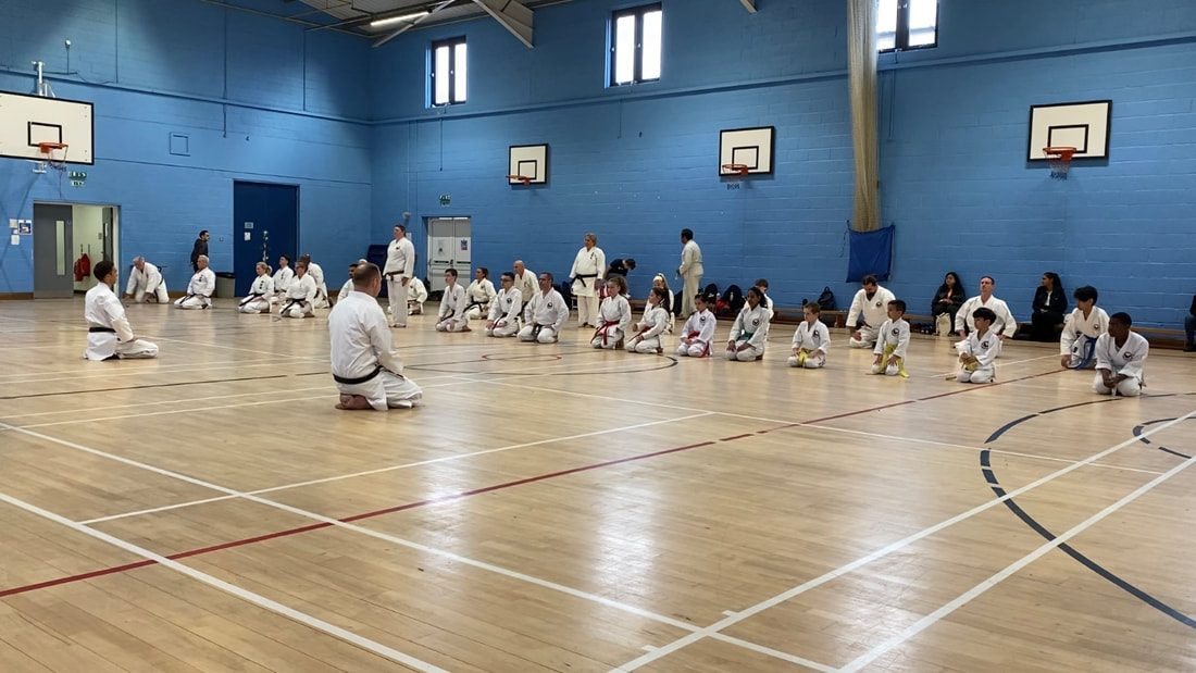 A class seated in rows on the hall floor facing the instructor